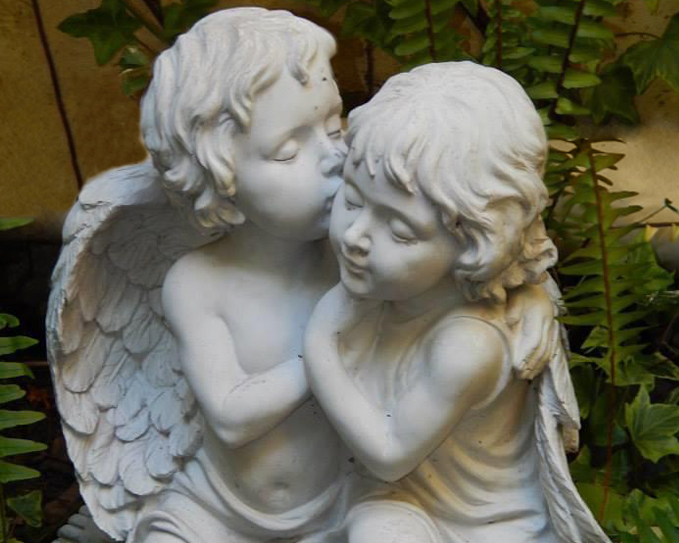 Escultura de dos ángeles de piedra entre helechos