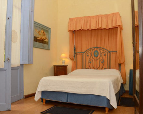 Habitación con cama de hierro, cortinas color durazno y colcha blanca