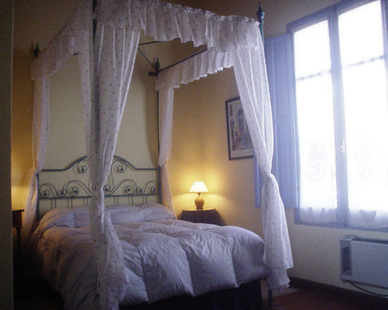 Habitación con cama con baldaquino blanco junto a una ventana luminosa
