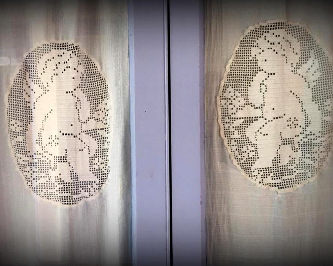 Cortinas de encaje con ángeles bordados frente a una ventana