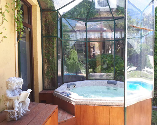 Jacuzzi bajo una pérgola de vidrio rodeada de plantas